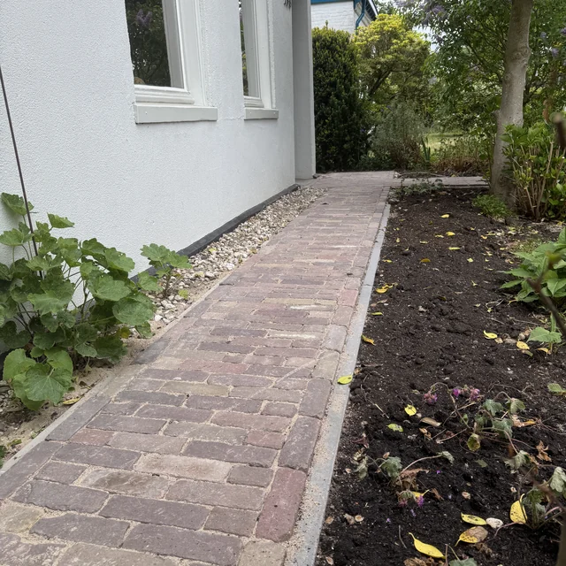 Tuinpad van gebakken klinkers langs de gevel, met border ernaast