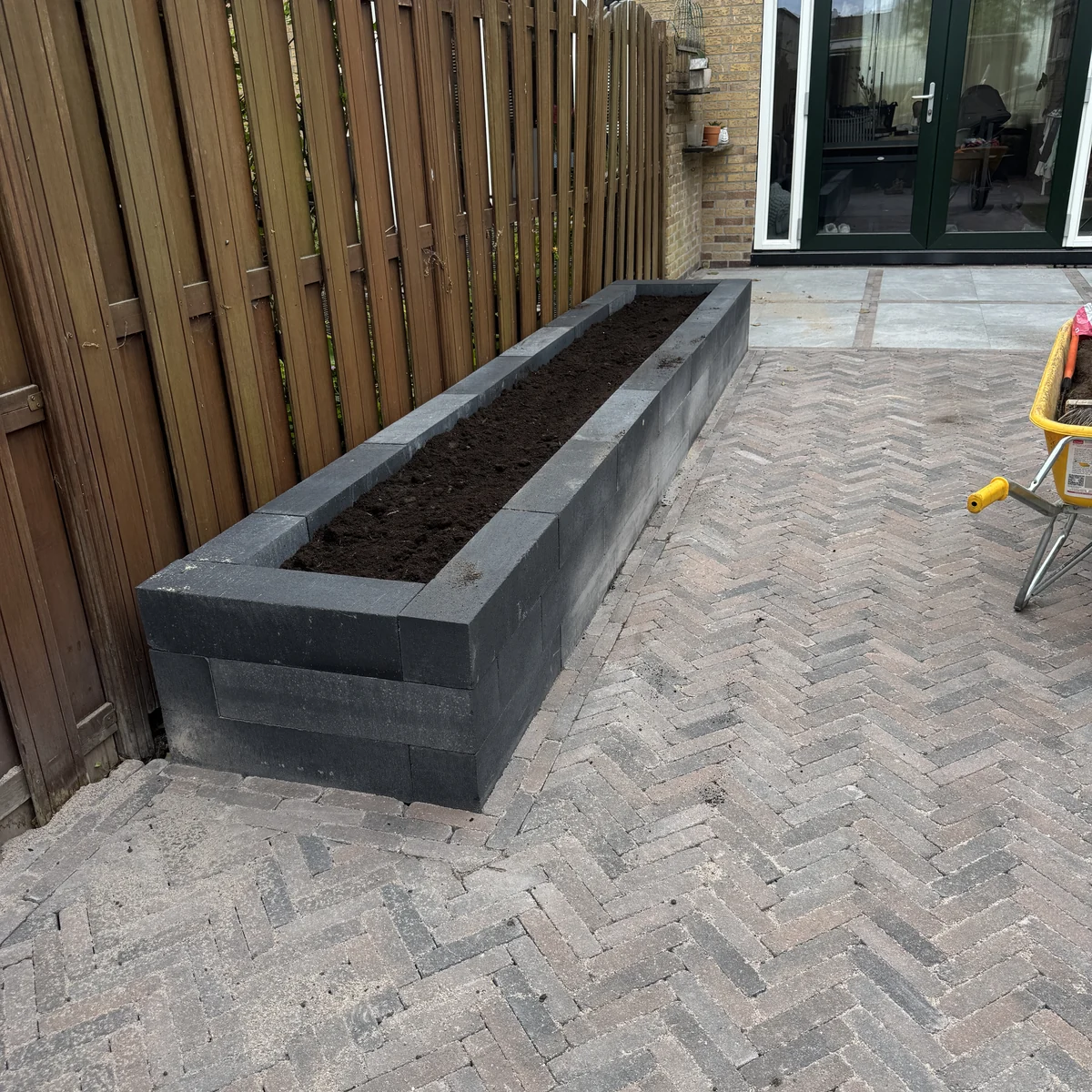 Achtertuin in keperverband met een verhoogde plantenbak van antraciet betonblokken langs de schutting